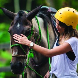 a girl wearing a helmet petting a horse