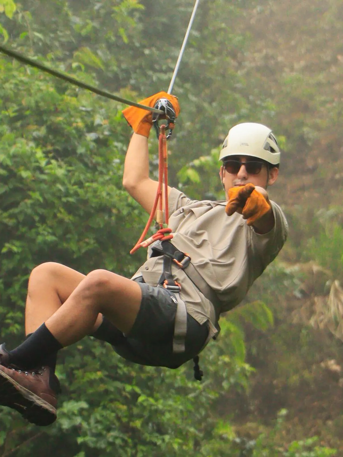 Person ziplining through a misty forest, wearing a helmet and gloves.