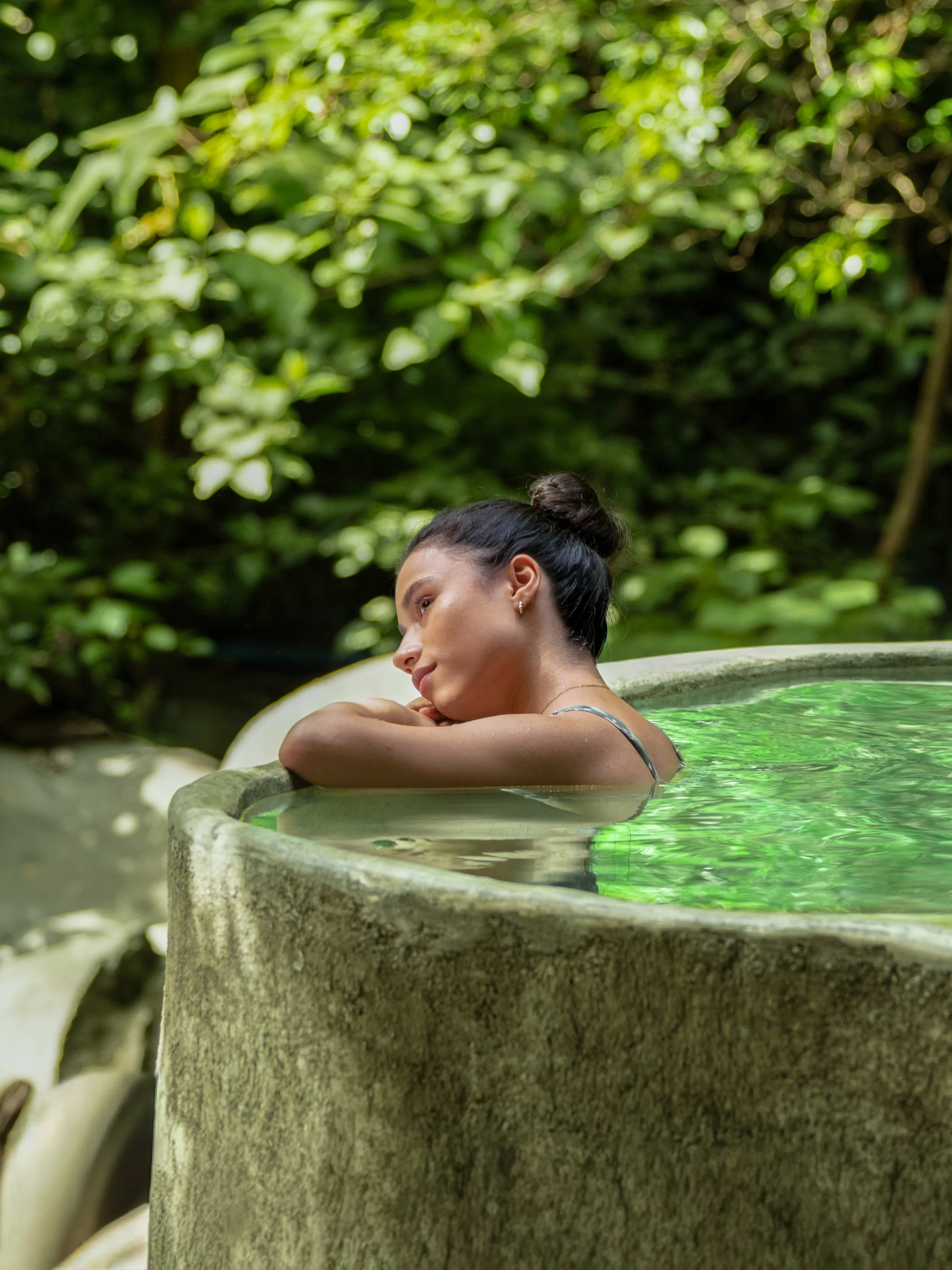 Woman relaxing in a stone hot tub surrounded by lush greenery.