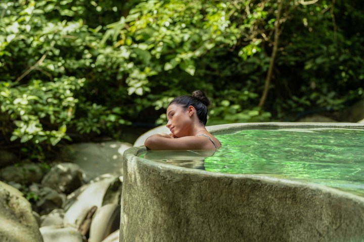 Woman relaxing in a stone hot tub surrounded by lush greenery.