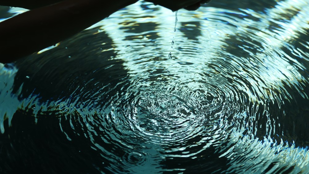 Hand above water creating ripples with dripping droplets.