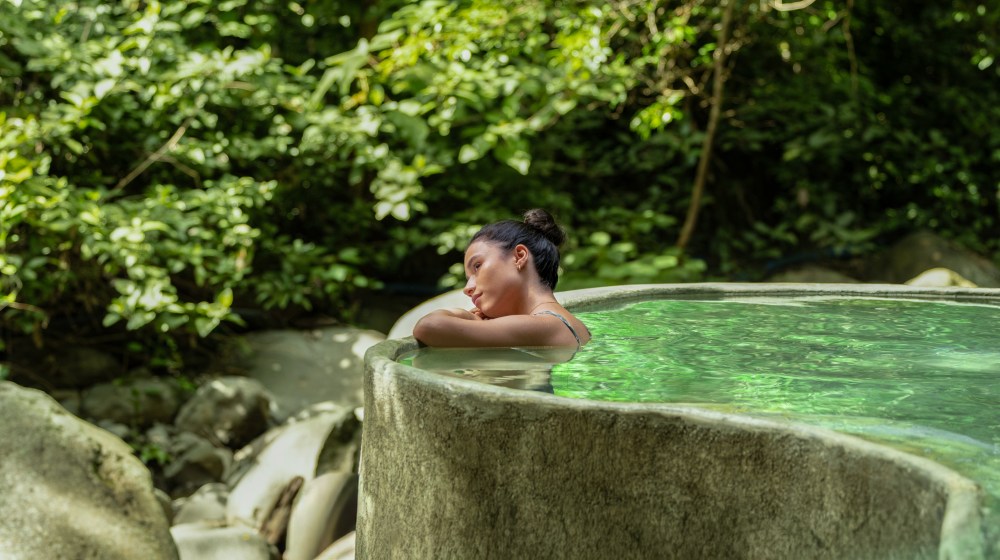 Person relaxing in a lush green outdoor hot spring.