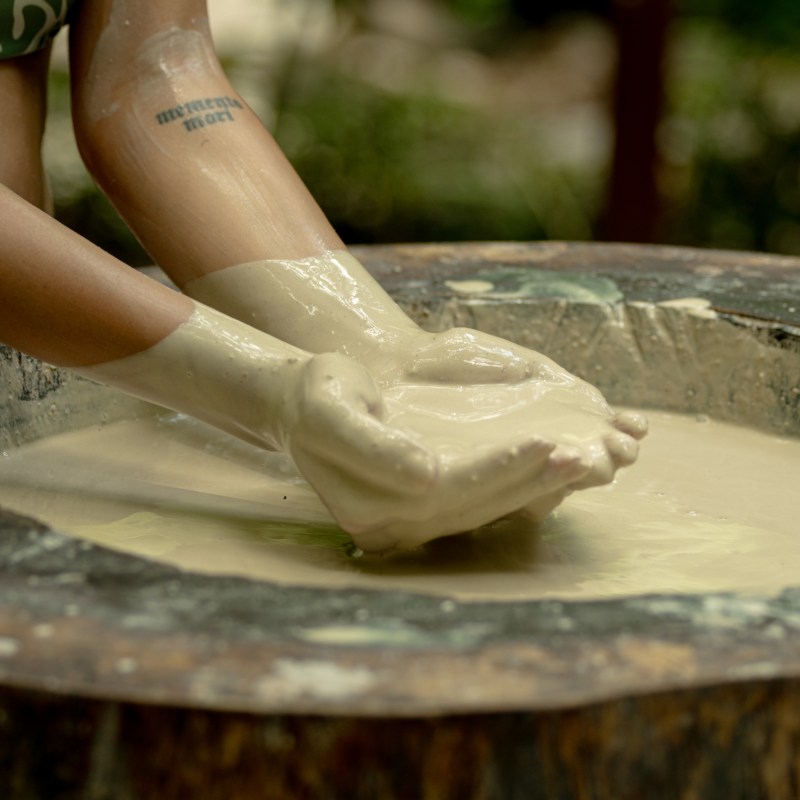 Person's arms submerged in creamy mixture inside a large wooden bowl.